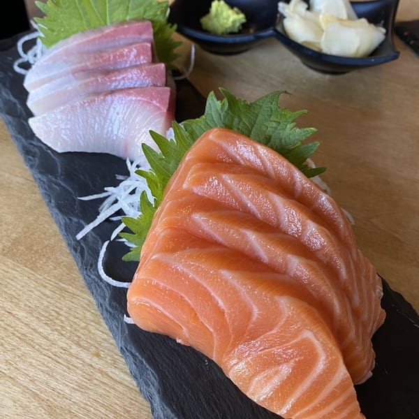 Fresh salmon and white fish sashimi on a black slate, with wasabi and ginger in the background.