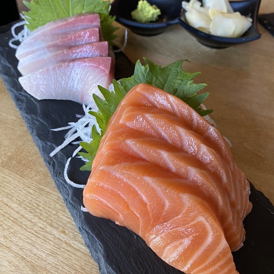 Fresh salmon and white fish sashimi on a black slate, with wasabi and ginger in the background.