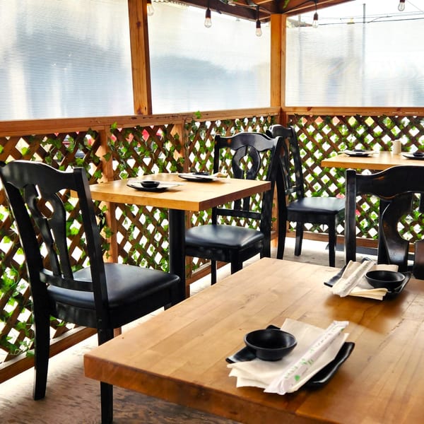 Kazoku Sushi's outdoor patio with wooden tables, black chairs, and lattice walls adorned with ivy.