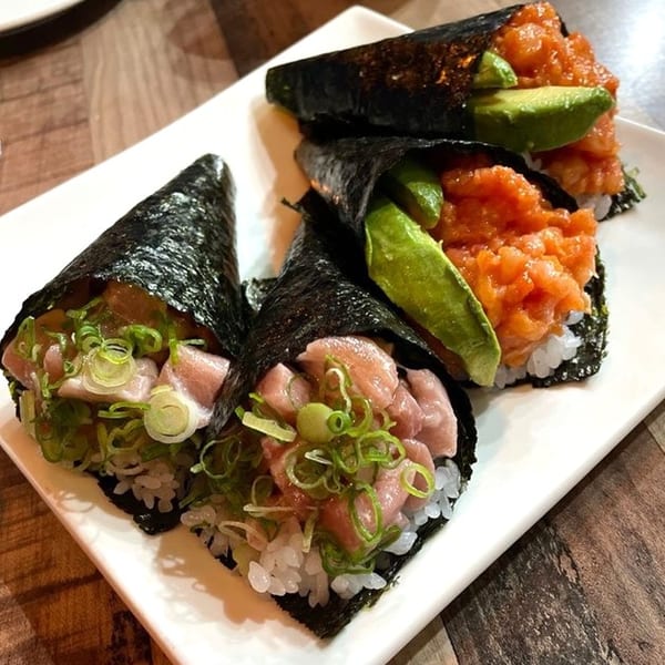 Four Kazoku Sushi hand rolls with tuna, salmon, avocado, and green onions on a white plate.