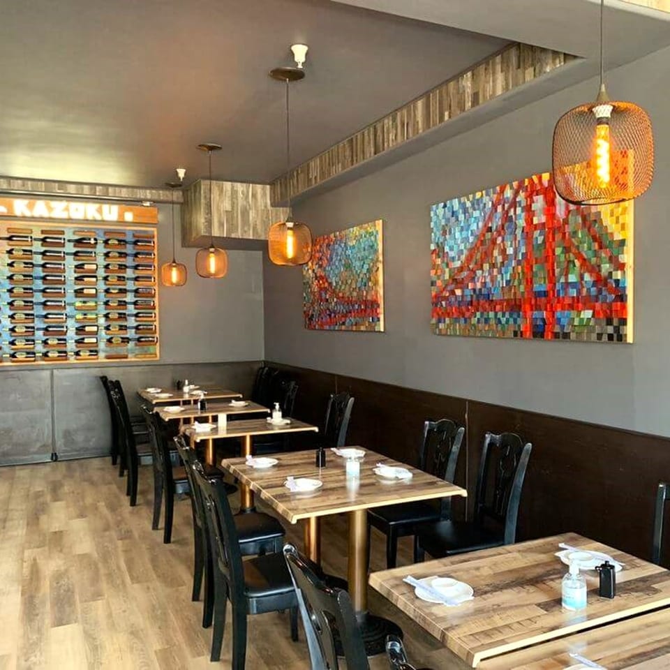 Interior of Kazoku Sushi restaurant with empty tables, modern art, and a wine display.
